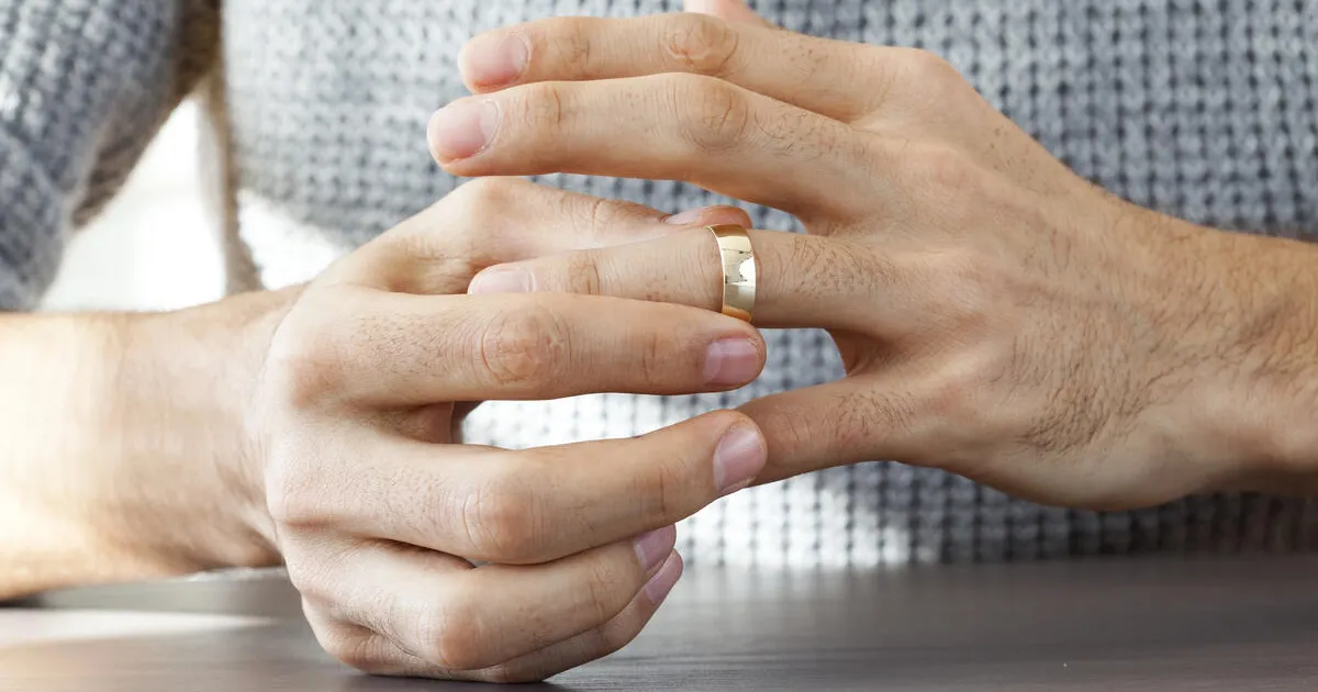 Close-up of a man's hands as he slides a golden wedding band off of his finger, representing a divorce or separation.