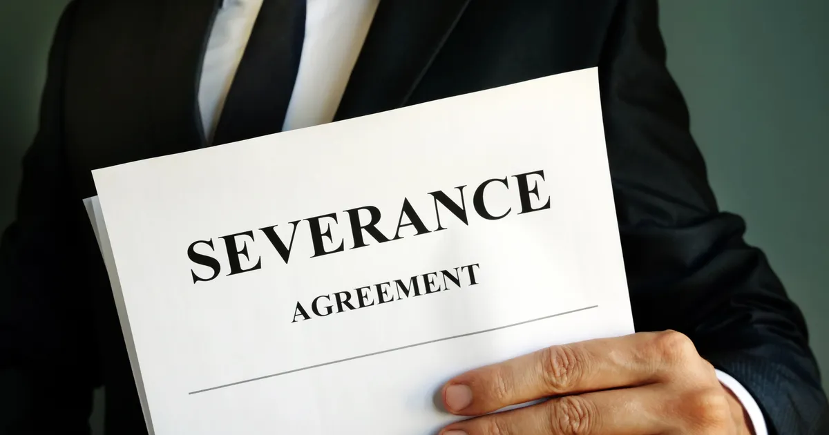 A person in a dark suit and tie holds a printed document titled Severance Agreement.