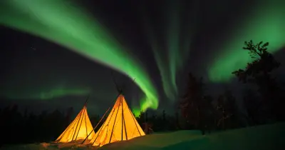 Green northern lights over two glowing tipis near Yellowknife, Northwest Territories