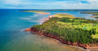 Aerial view of red sandstone cliffs, forest and green fields along the shore of Prince Edward Island
